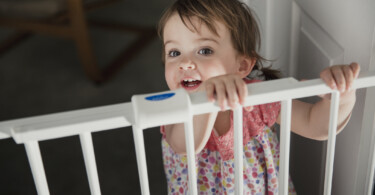 Kindersichere Wohnung - stehendes Mädchen an Türschutzgitter