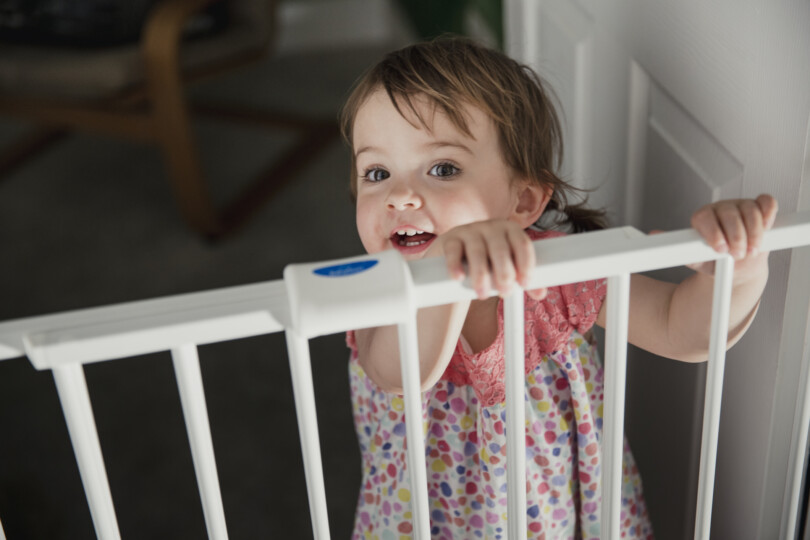 Kindersichere Wohnung - stehendes Mädchen an Türschutzgitter