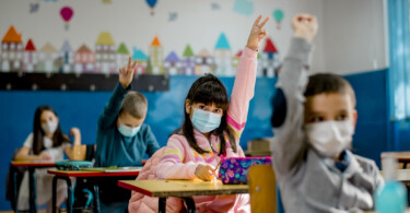 Mundschutz für Kinder - Kind meldet sich in der Klasse