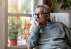 Coronabedingte psychosomatische Erkrankungen - Mann sitzt traurig am Fenster