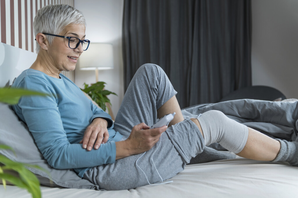 Frau nutzt TENS-Gerät auf dem Sofa